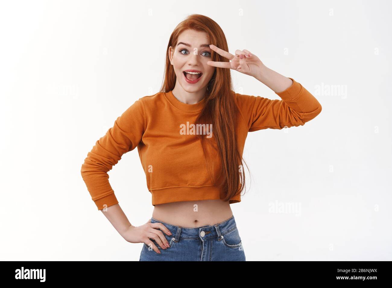 Cute and silly ginger girl in orange cropped top, jeans, hold hand