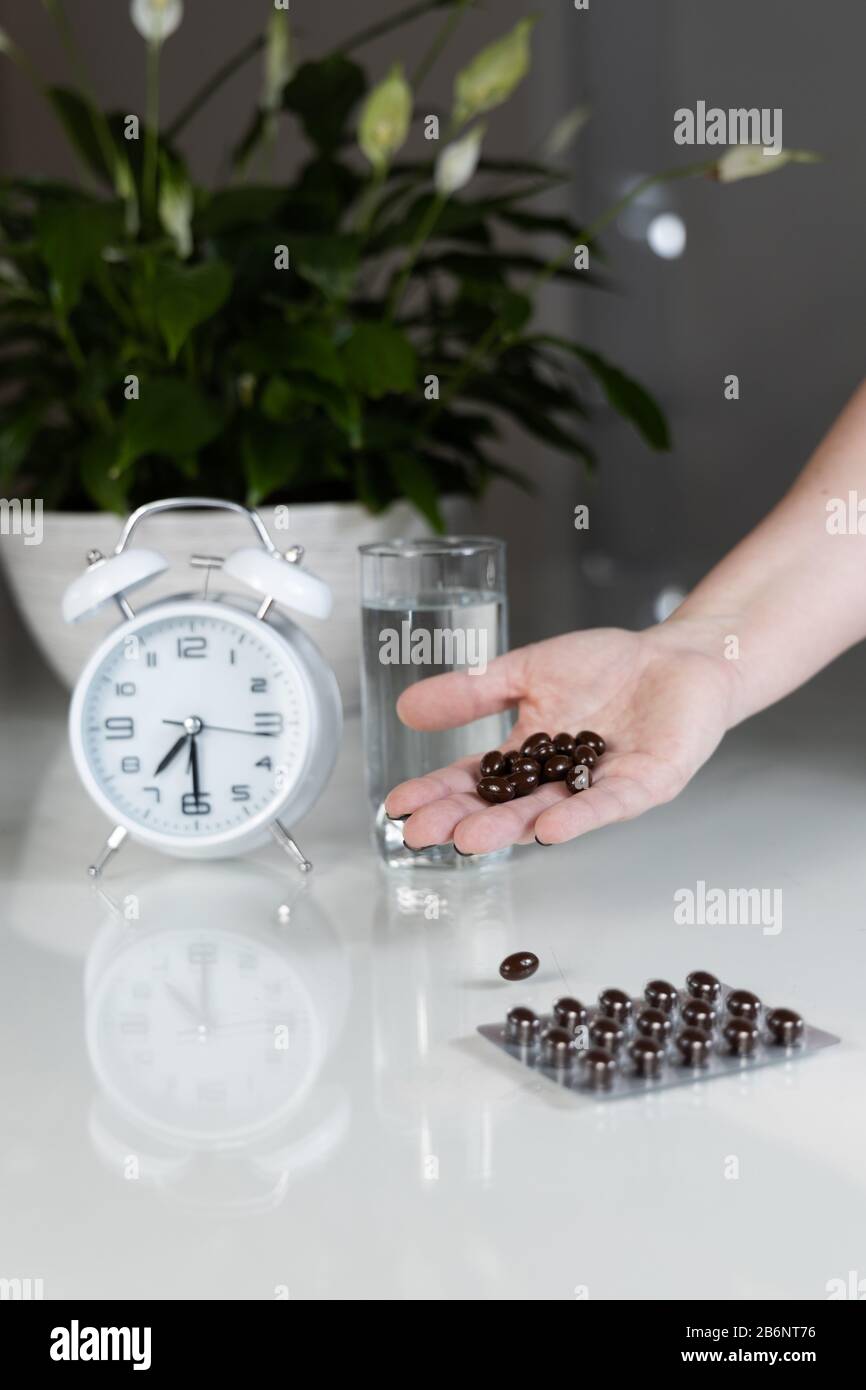White alarm clock and medical pills with a glass of water on the table. Healthcare and medicine. Vitamins and mineral supplements in capsules. Stock Photo
