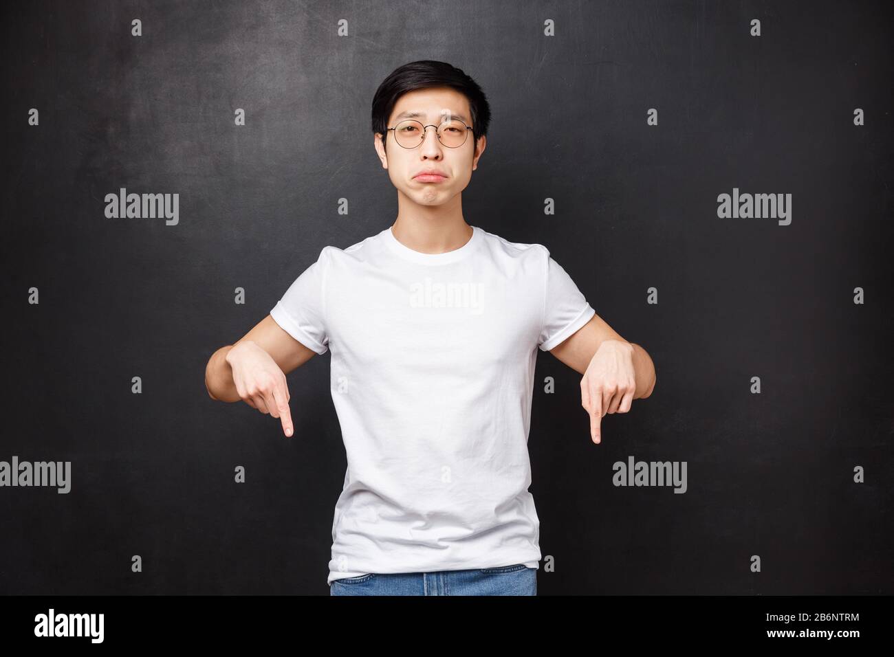 Miserable and gloomy upset cute asian guy sobbing look at camera with regret and sadness, pointing fingers down at something broken or upsetting, feel Stock Photo
