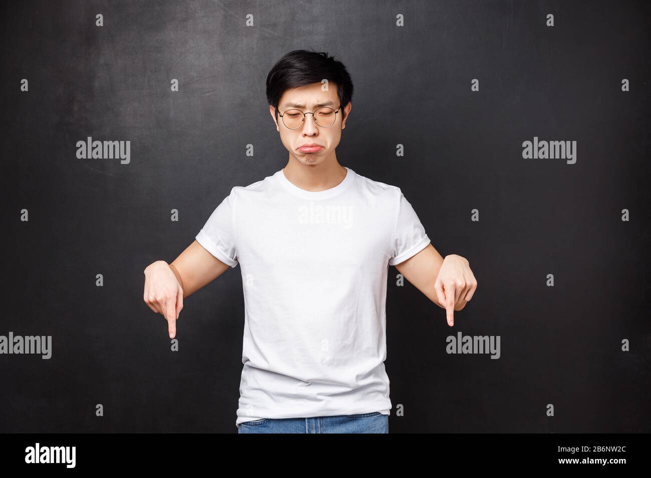 Whining and sobbing miserable upset asian guy feel gloomy, grimacing uneasy and distressed, looking pointing down, losing didnt won prize, regret of Stock Photo