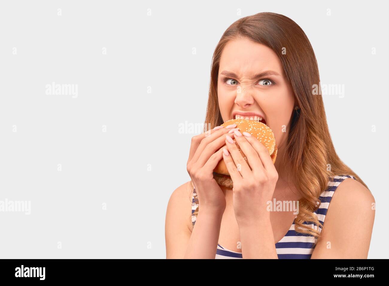 Cute girl quickly eats Burger, wrinkling nose Stock Photo