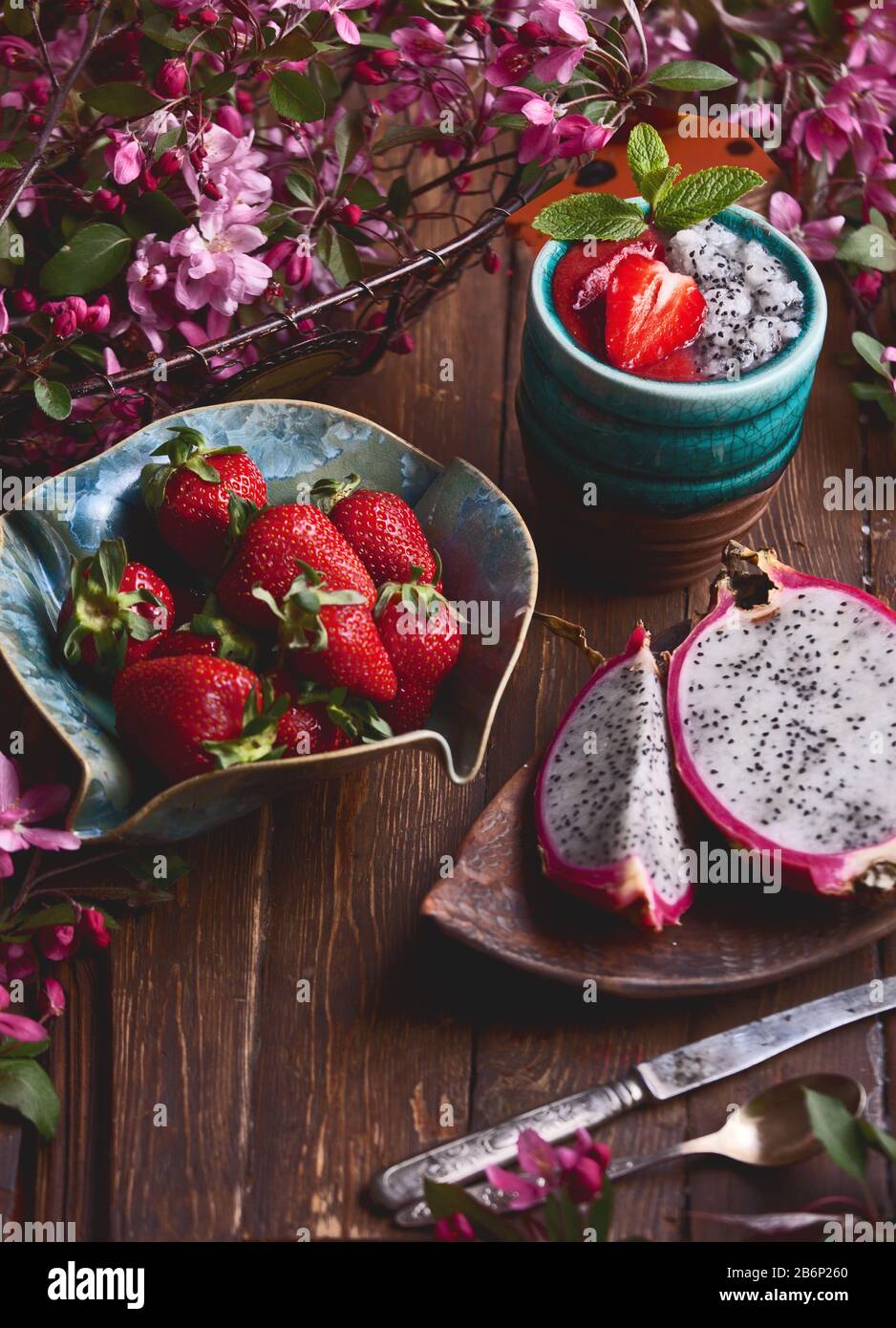 flatlay food background - empty dark wooden board with dragon fruit, strawberries, fresh smoothie and pink flowers, copy space for text Stock Photo