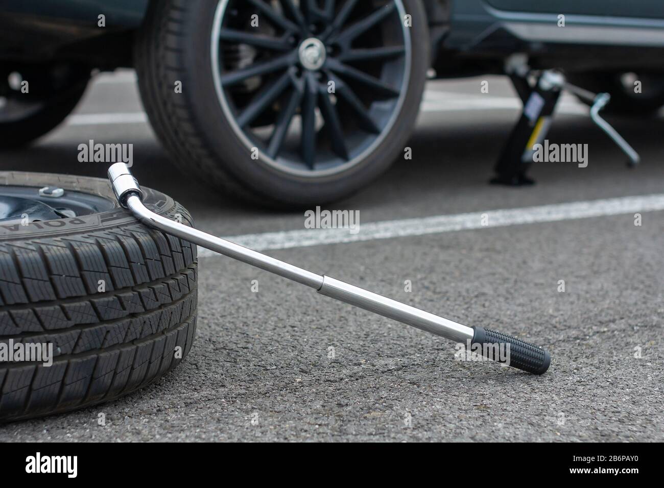 A flat tire car wheel and screwdriver are on a asphalt road on the broken Skoda Rapid background. Jack is lifting up a vehicle. Automobile service Stock Photo