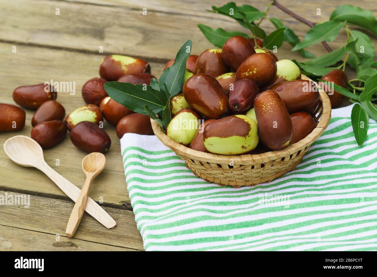 Braided Cup with ripe fruits of the jujube (lat. Ziziphus jujuba) on an old wooden table. Two wooden spoons and a striped napkin Stock Photo