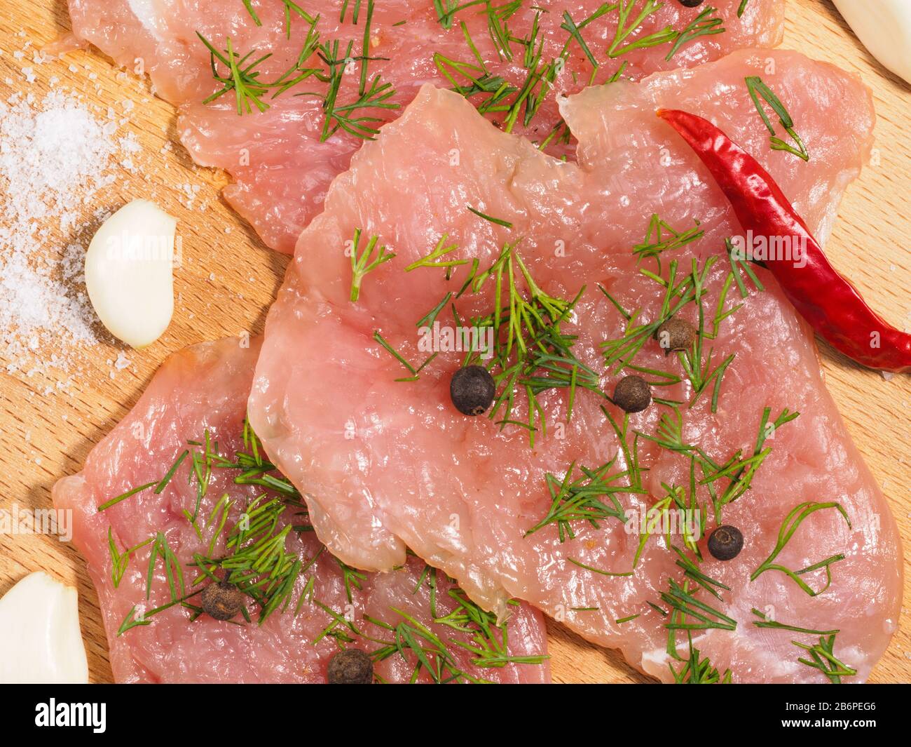 Sliced pieces of meat turkey game filet, garlic, salt, fennel, red chili pepper, allspice on wooden cutting board. Healthy eating concept. Macro photo Stock Photo