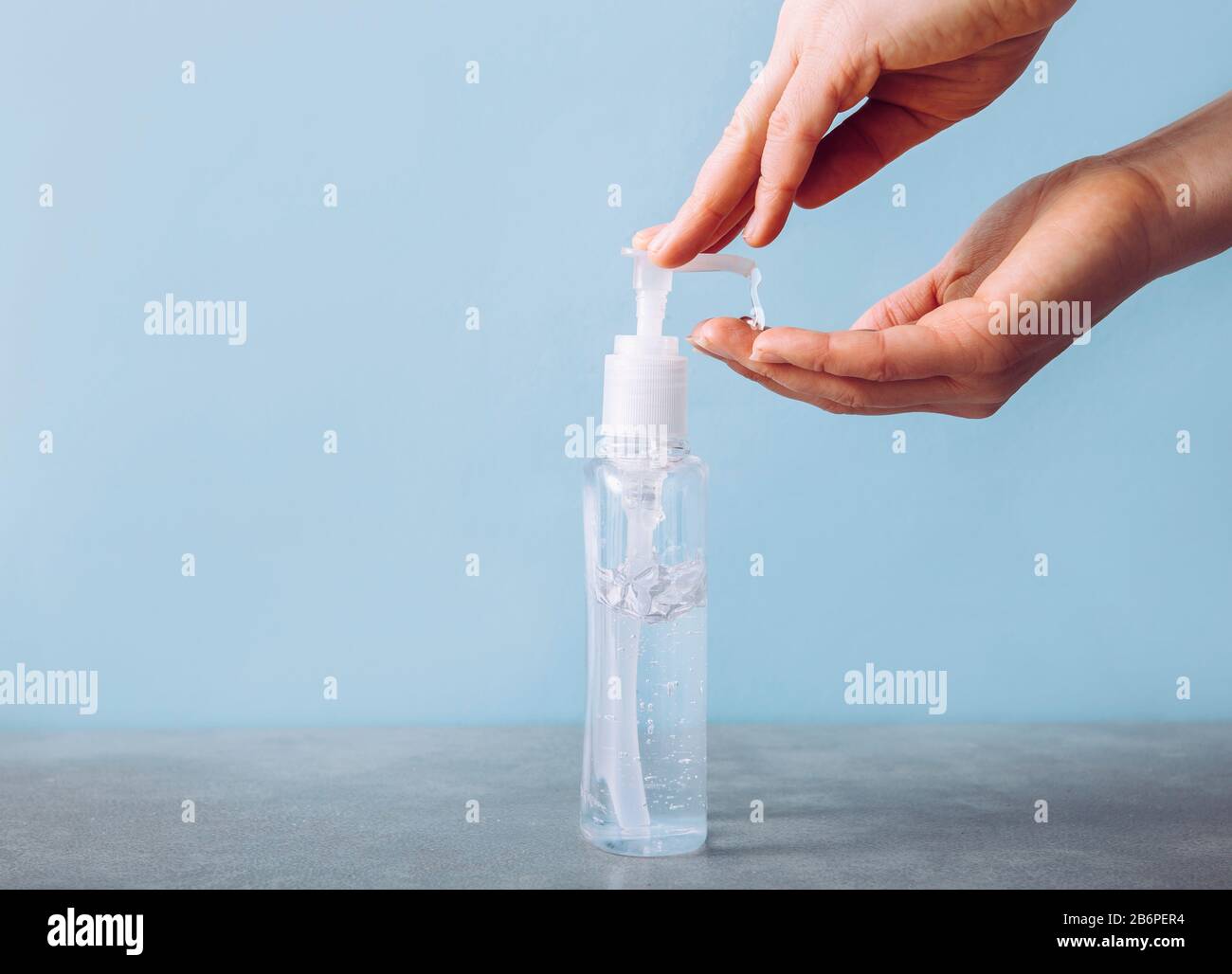 Close up view of woman using hand sanitizer dispenser, blue clean minimalist background. Health concerns concept. Stock Photo