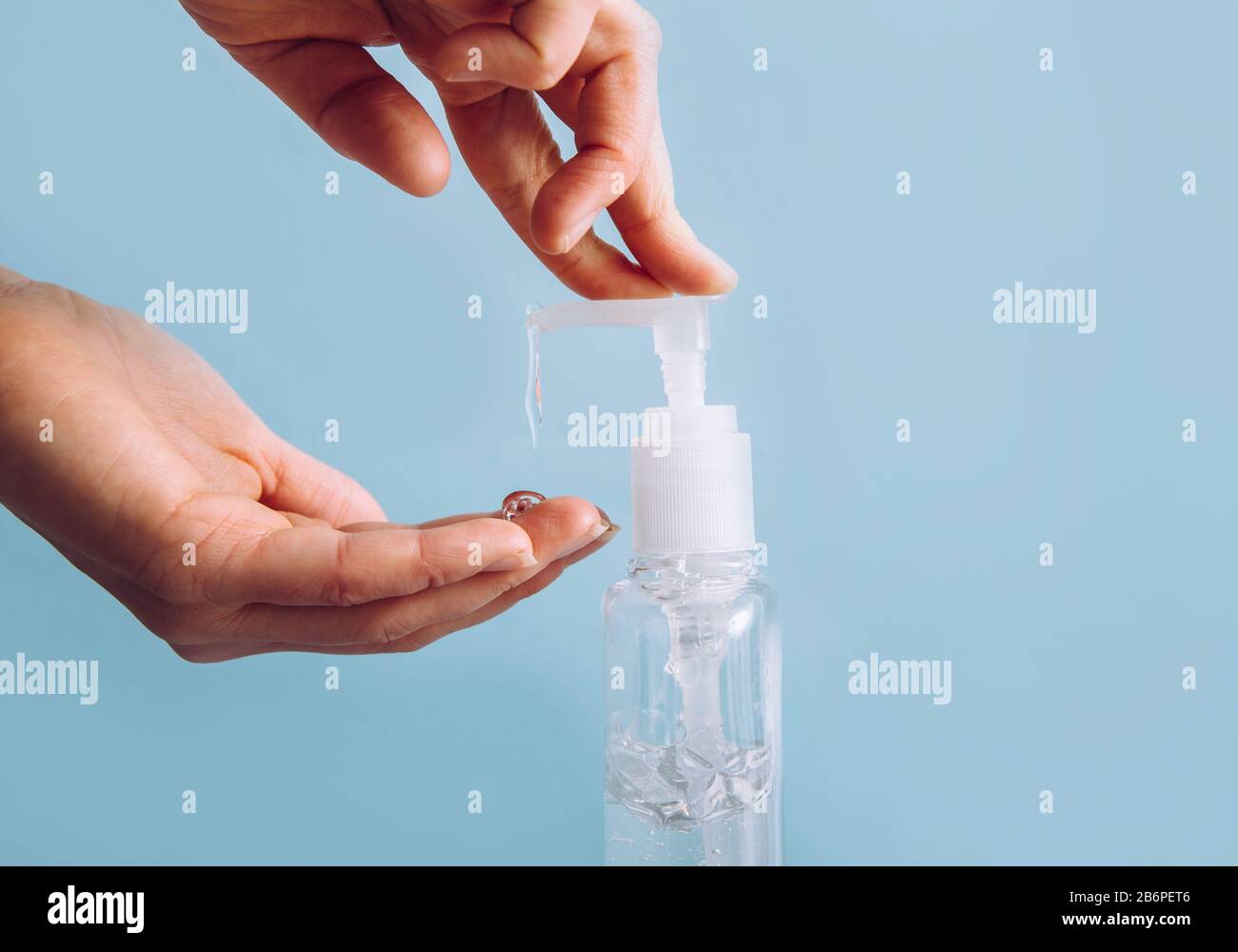 Close up view of woman using hand sanitizer dispenser, blue clean minimalist background. Health concerns concept. Stock Photo