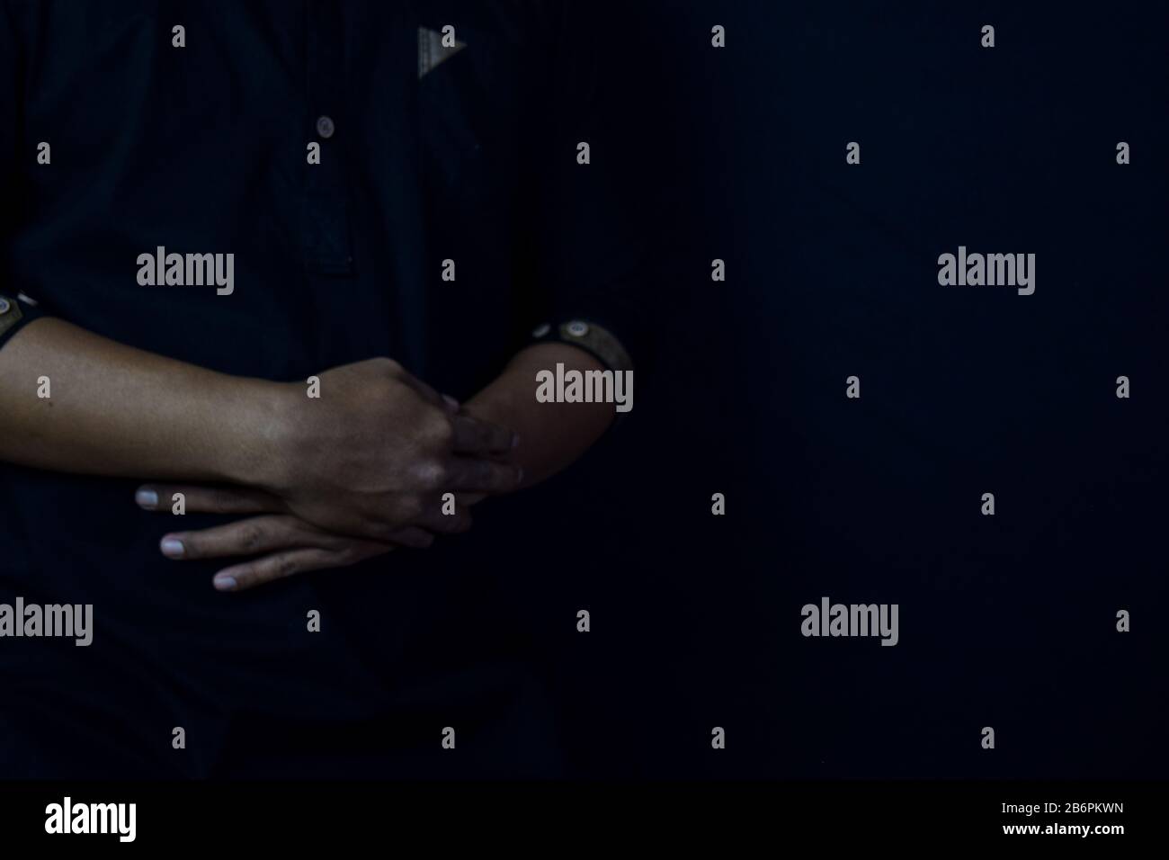 Young man praying with arms across posture. Islamic praying concept on black background. Selective focus on finger Stock Photo