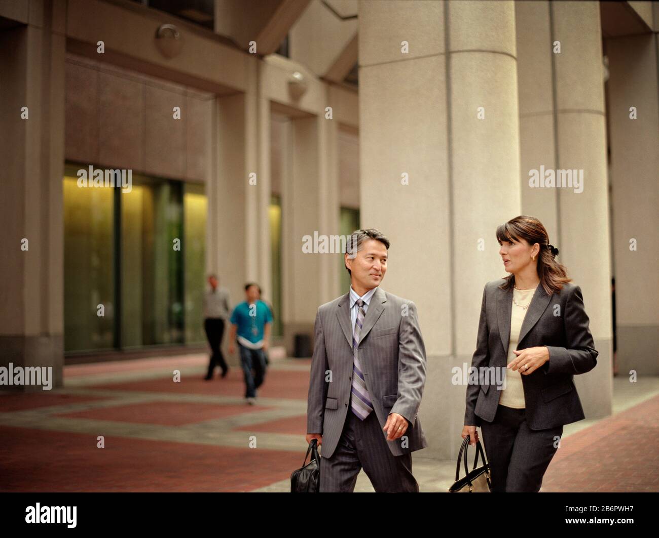 Mid-adult business woman walking on the street with a mid-adult male colleague. Stock Photo
