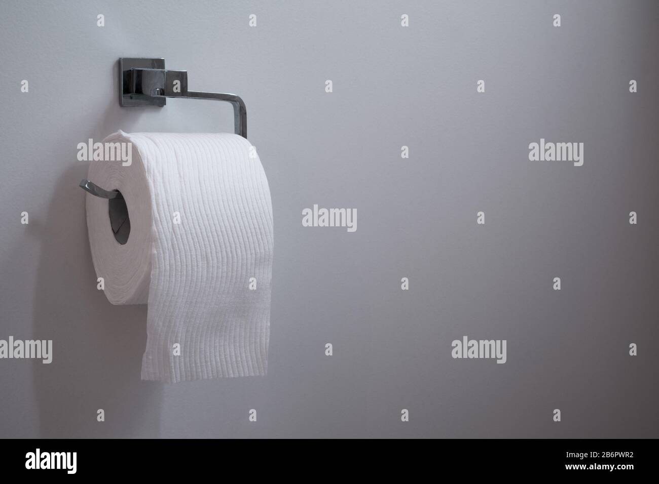 White toilet roll paper on chrome holder against a white wall neutral background copy space Stock Photo