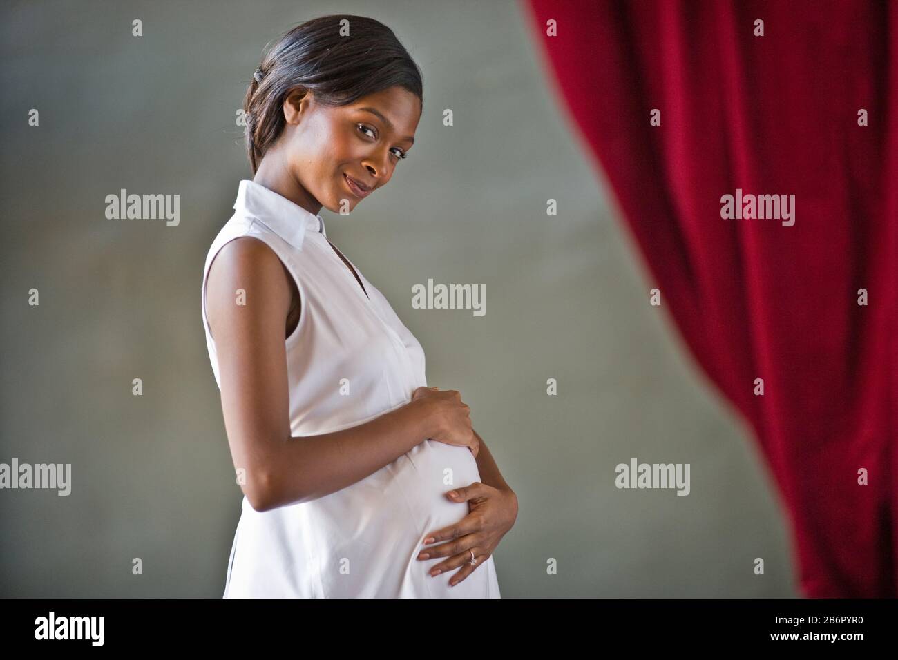 Portrait of a pregnant mid-adult woman standing with her hand on her belly. Stock Photo