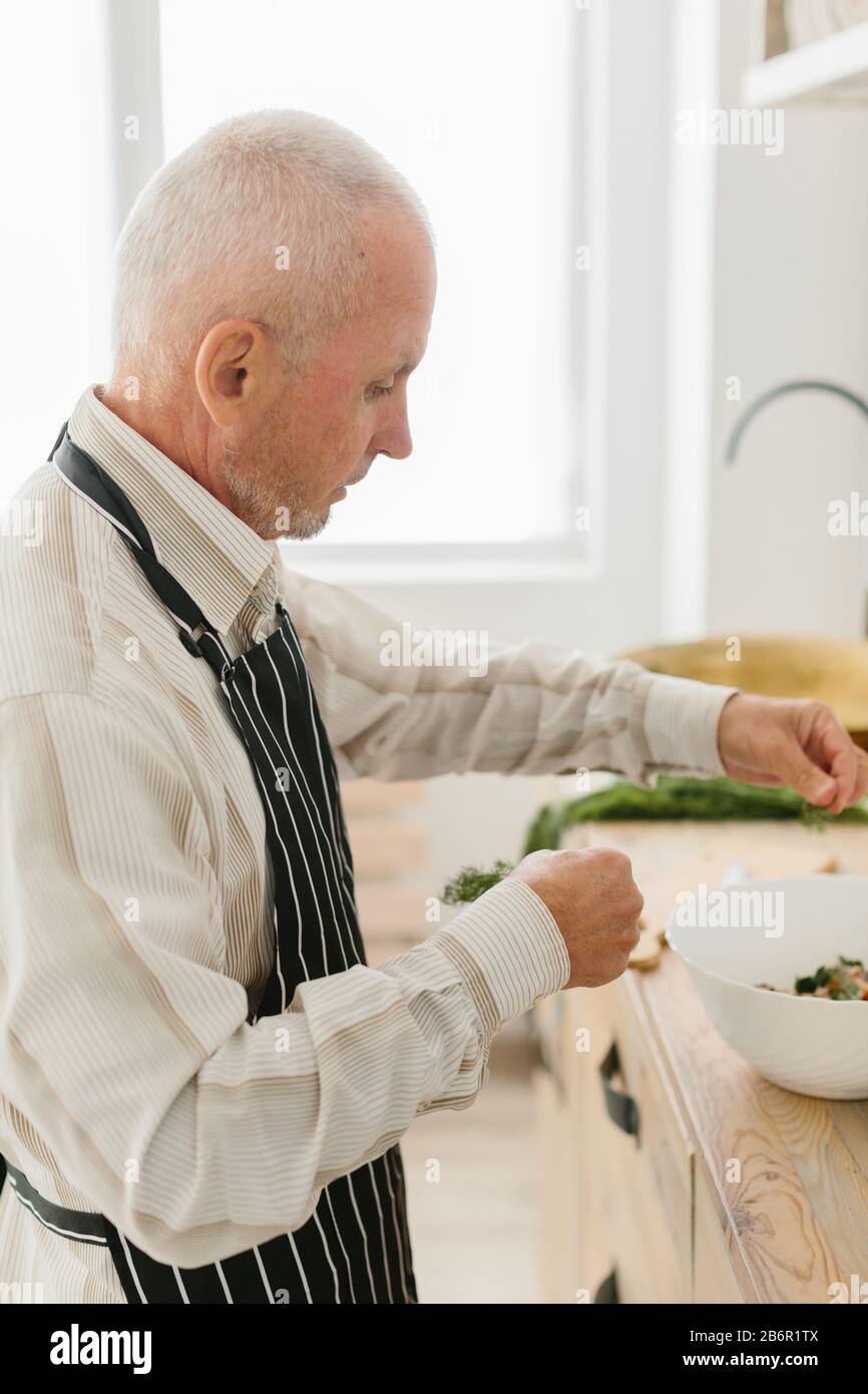 senior father prepares a salad in the kitchen Stock Photo