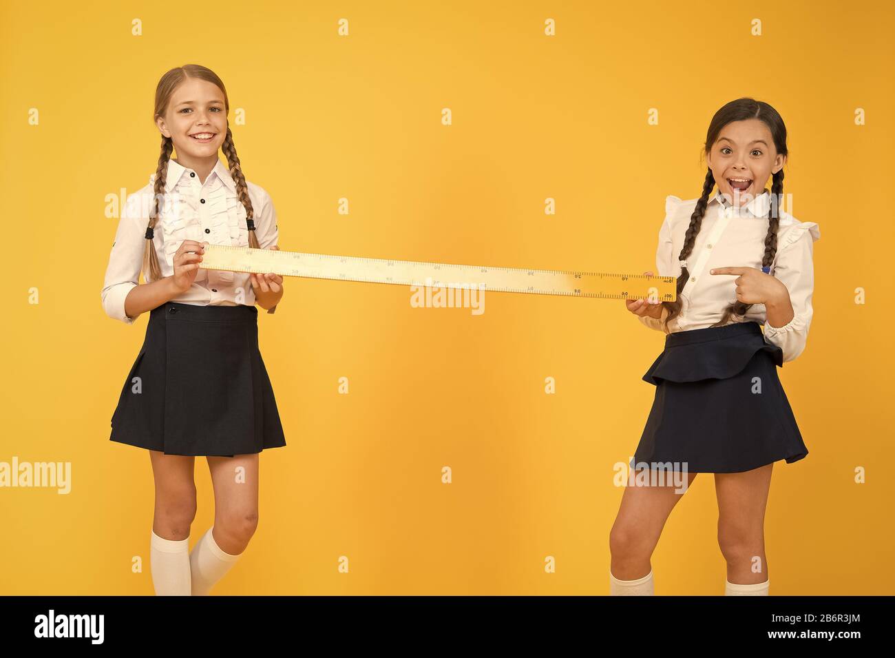 Close or far. Measuring skills. Measuring distance. Measuring equipment. Kids students study math. Knowledge day. Schoolgirls school uniform hold big ruler. Geometry school lesson. Teamwork concept. Stock Photo