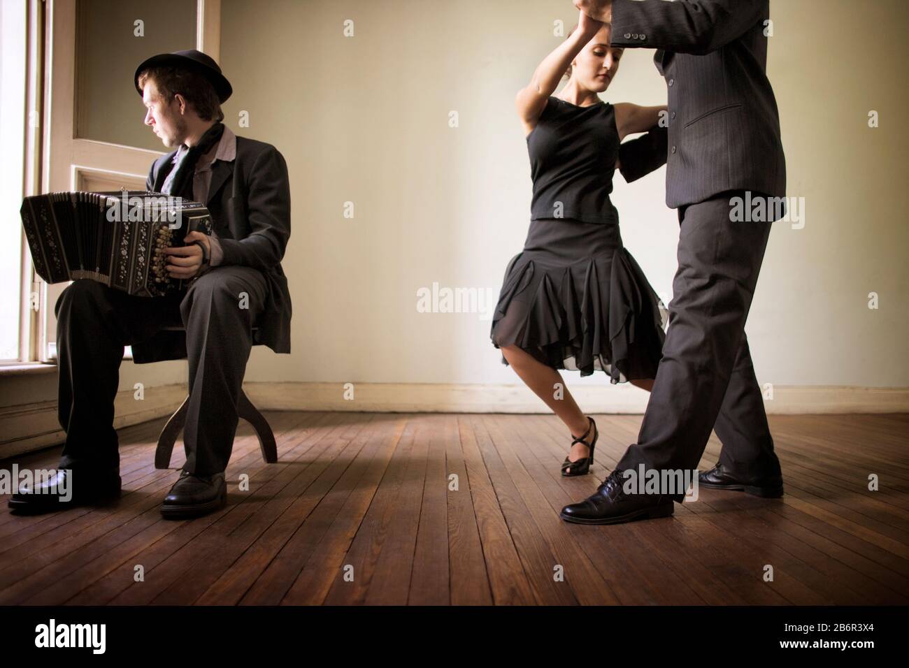 Side view of two people dancing as a man plays harmonium. Stock Photo