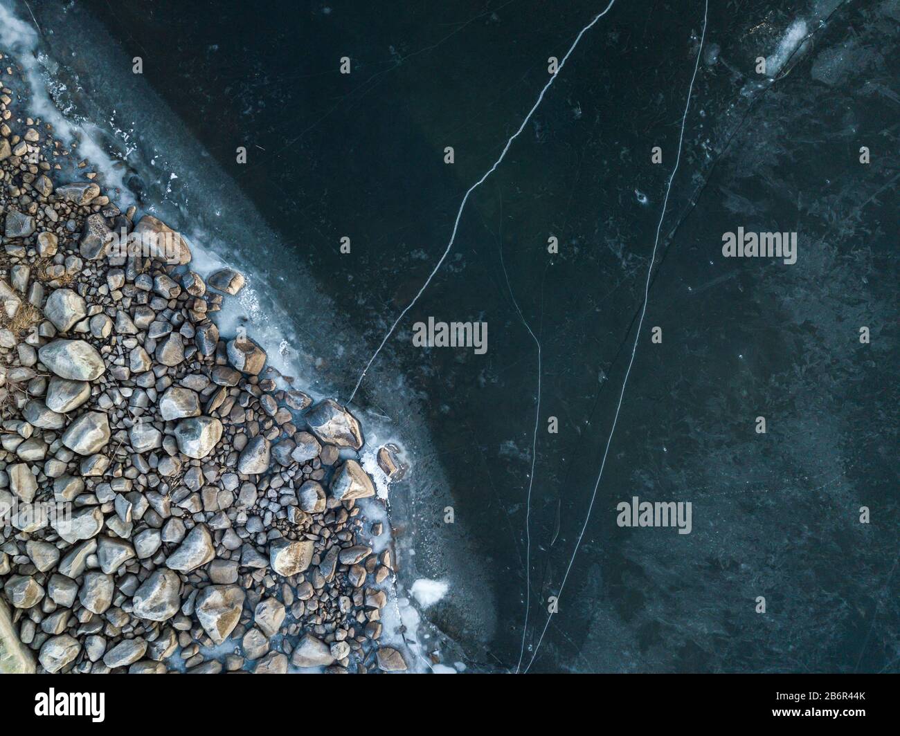 Stony shore with clear ice cover. Vertical aerial shot. Stock Photo