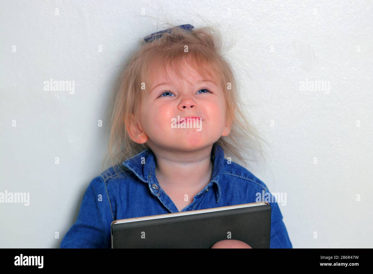 A little girl pulling silly faces while using her tablet. Stock Photo
