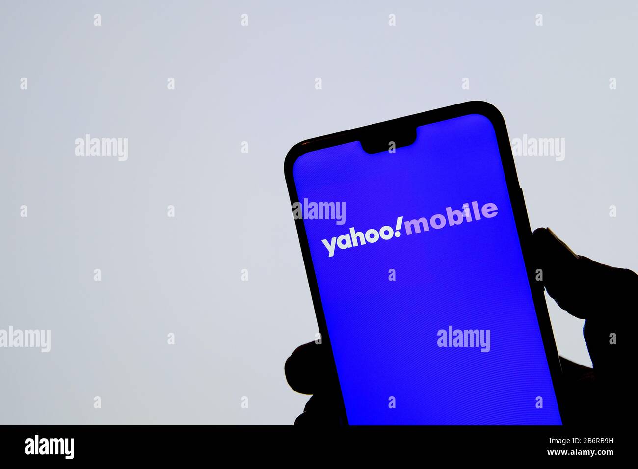 Stone / United Kingdom - March 11 2020: Yahoo! Mobile logo on the silhouette of smartphone hold in a hand and blurred white background. Stock Photo