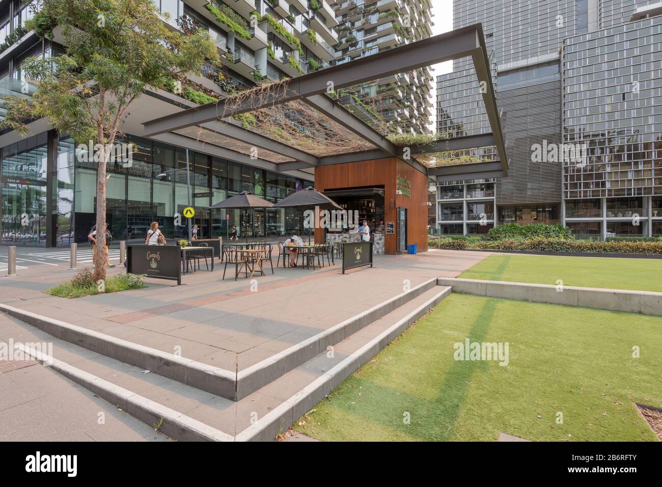 Green vines grow across a large trellis above an outdoor cafe beside a large grassed area in the centre of the Central Park development in Sydney. Stock Photo