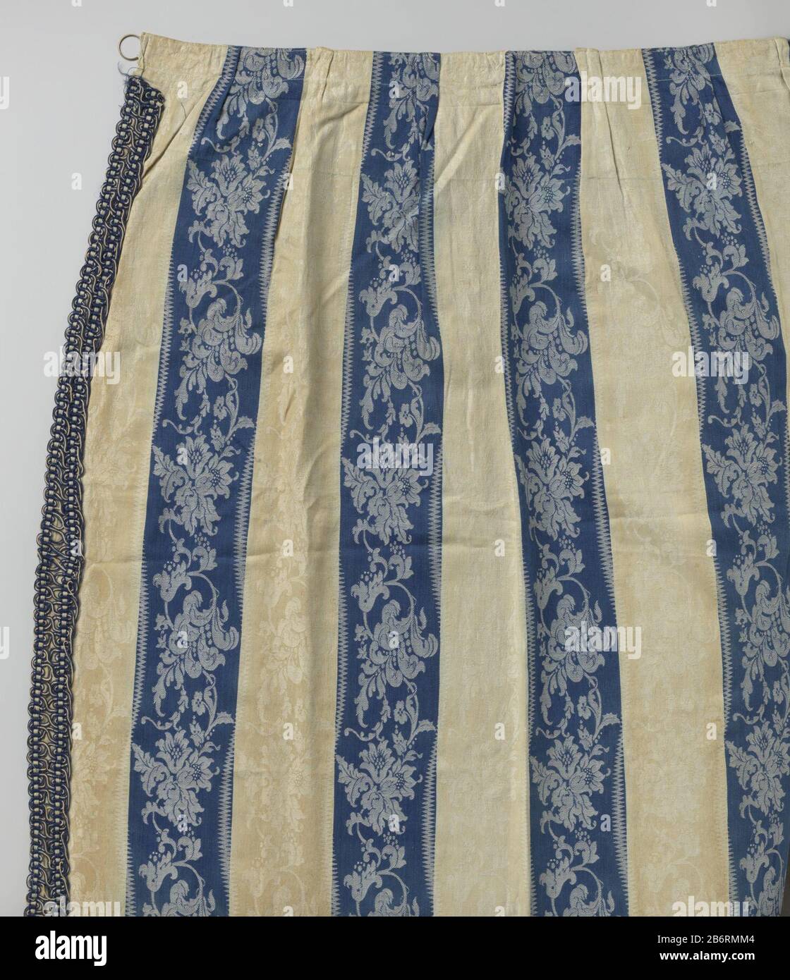 Gordijn van blauw en wit gestreept linnendamast Gordijn van blauw en wit  gestreept linnendamast. De blauwe en witte strepen hebben beide een lopend  patroon van bloemenranken; de blauwe in lichtblauw, de witte