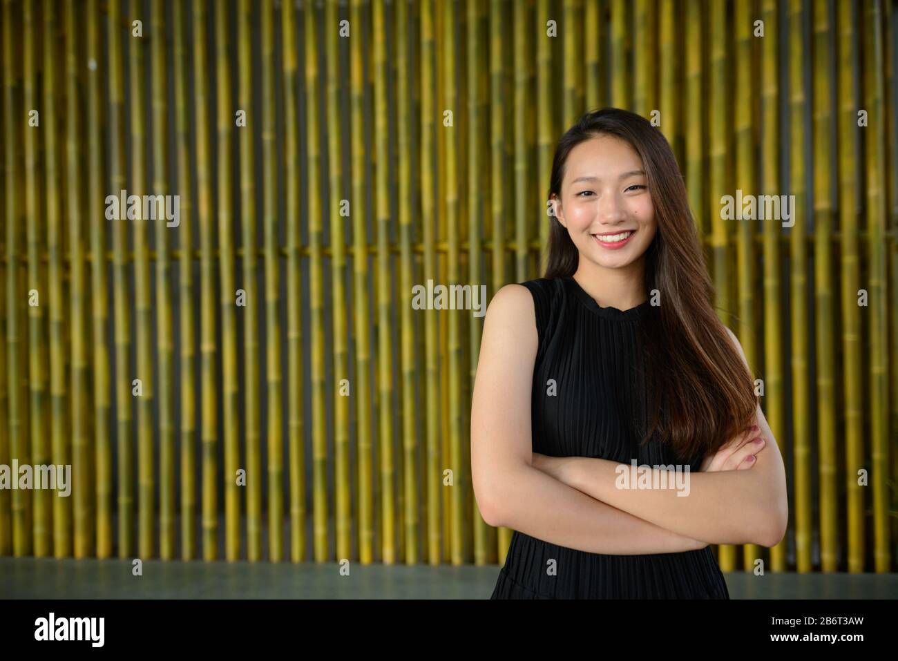Happy young beautiful Asian businesswoman smiling with arms crossed ...
