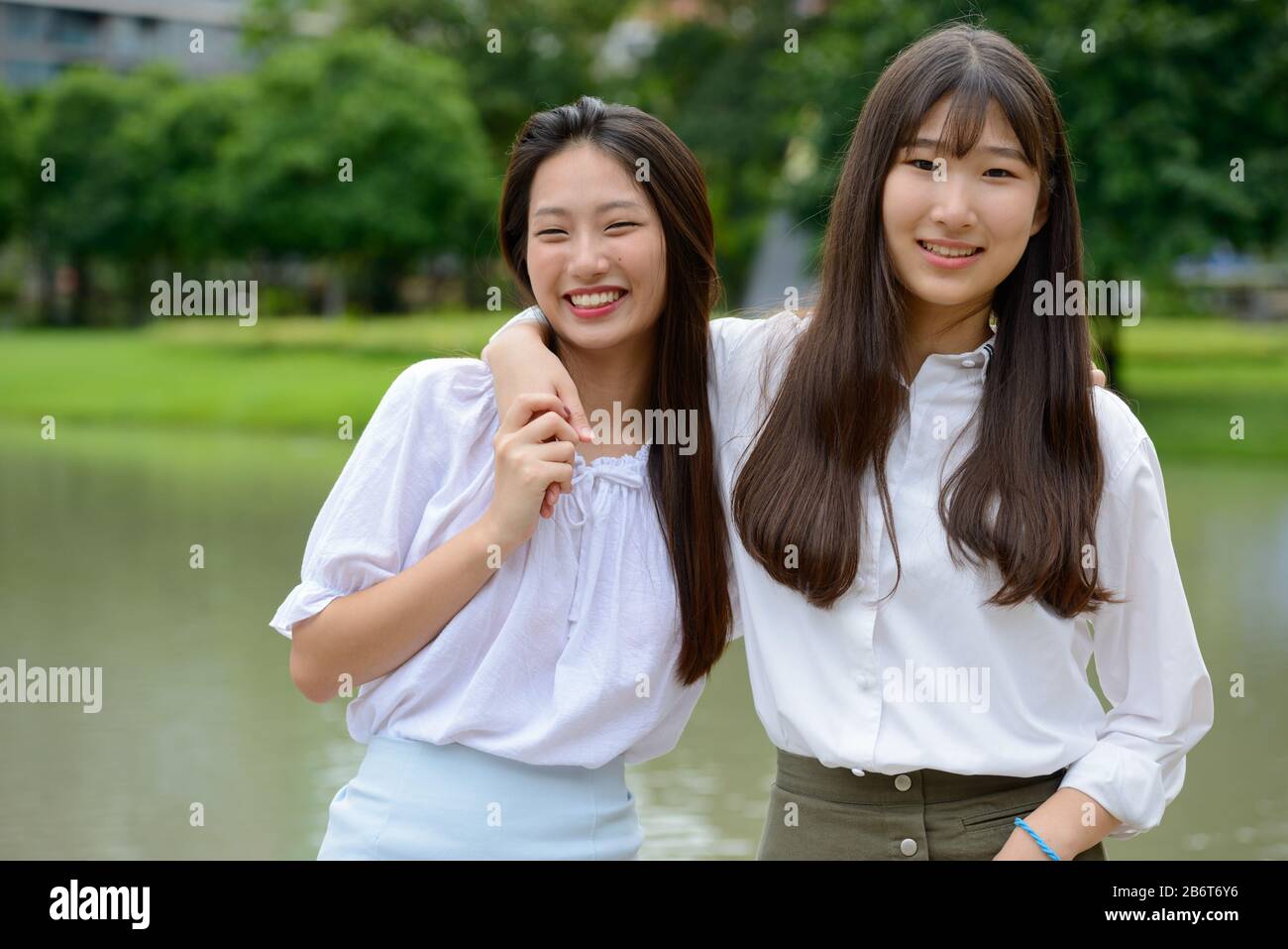 Two happy young beautiful Asian teenage girls bonding together at the park Stock Photo