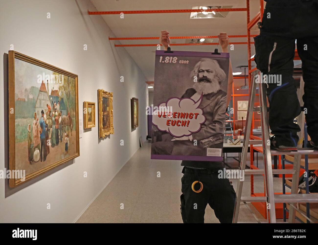 Bonn, Germany. 11th Mar, 2020. An employee of the Bundeskunsthalle hangs up a poster with the picture of Karl Marx. The exhibition 'Wir Kapitalisten - Von Anfang bis Turbo' (We Capitalists - From the Beginning to Turbo) can be seen at the Bundeskunsthalle from 13 March to 12 July 2020. Credit: Oliver Berg/dpa - ATTENTION: For editorial use only in connection with reporting on the exhibition/dpa/Alamy Live News Stock Photo