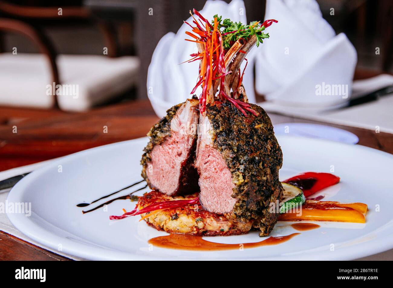 Roasted Lamb chop steak with crispy herb crust and grilled vegetables on white plate at dinner table Stock Photo