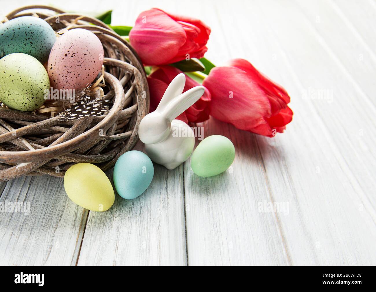 Easter background with colorful eggs in nest and pink tulips on a white ...