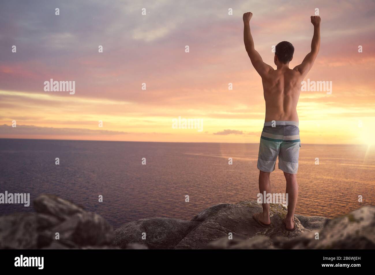 Man with raised arms standing on a cliff over the sea Stock Photo