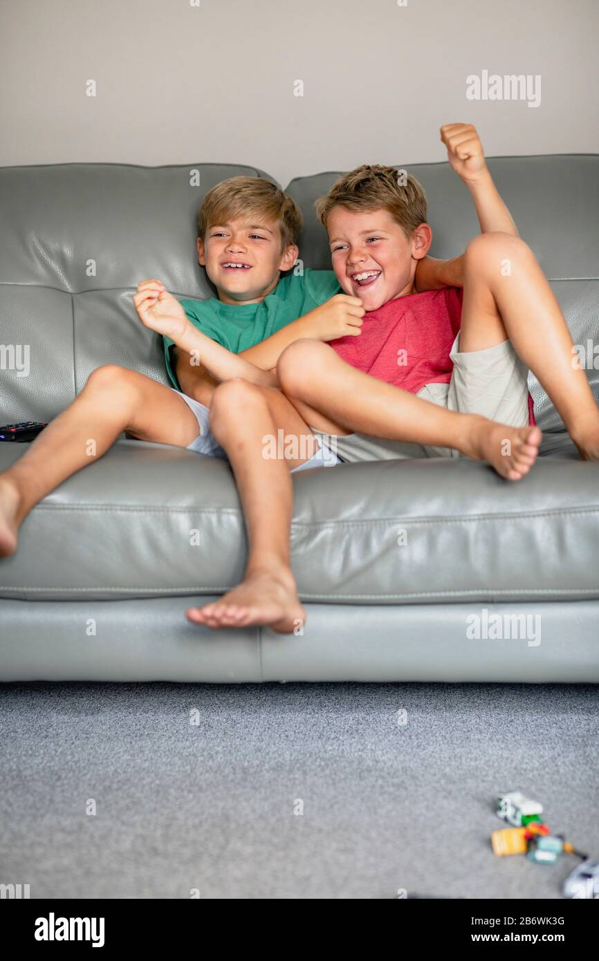 A shot of two young brother's sitting down on a couch together watching tv, they are wearing casual clothing. Stock Photo