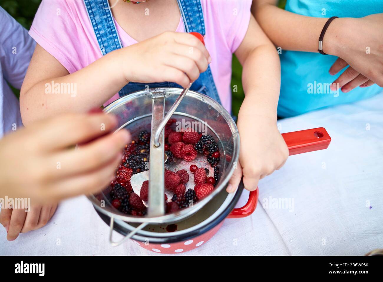 Children investigating food. Series: cooking jam. Mashing and sieving berries in a food mill. Learning according to the Reggio Pedagogy principle, playful understanding and discovery. Germany Stock Photo