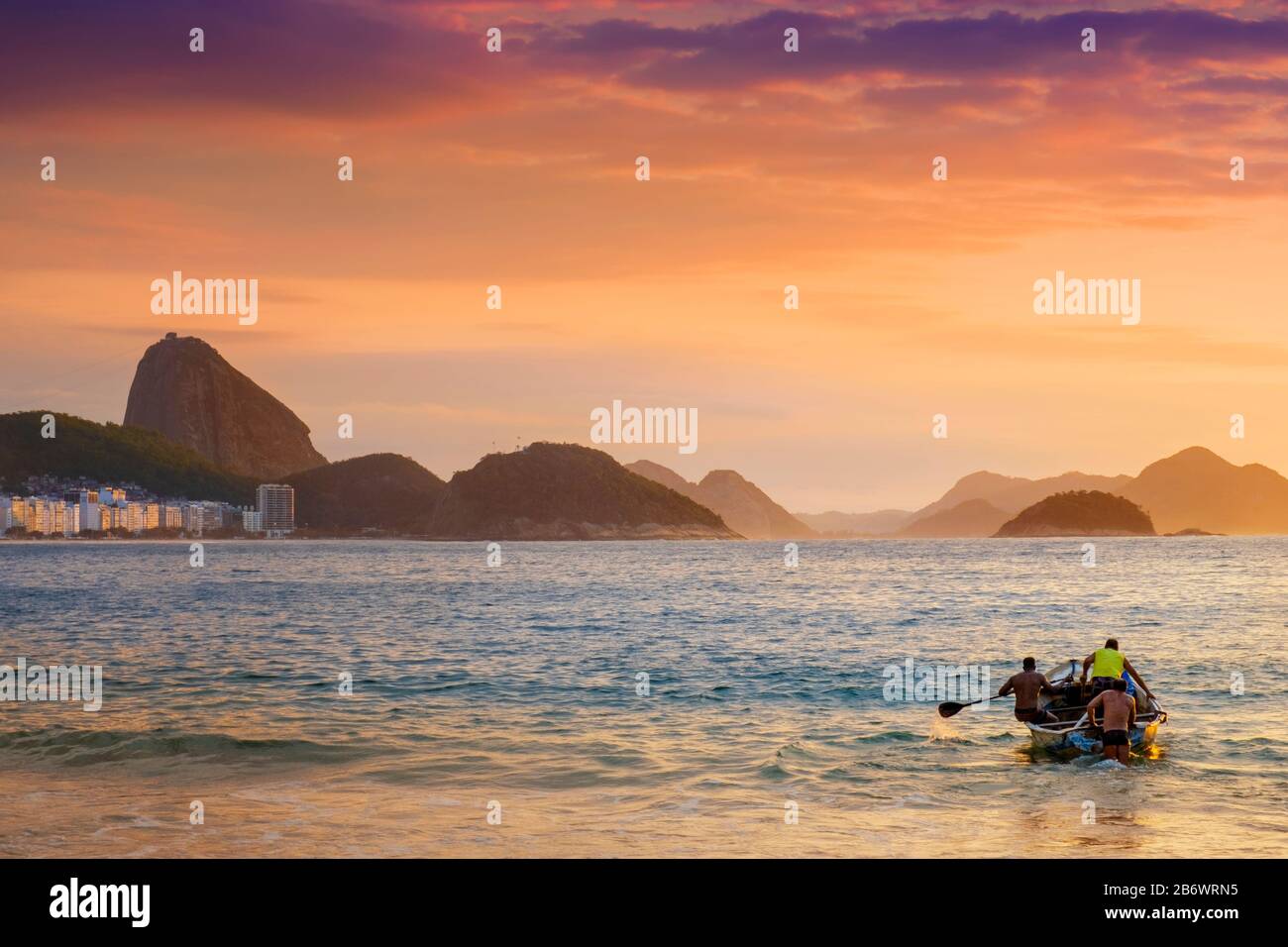 Brazil, Rio, Rio de Janeiro. Fishermen launching a boat with the Sugar Loaf, Leme hill and the mountains of Rio de Janeiro behind Stock Photo