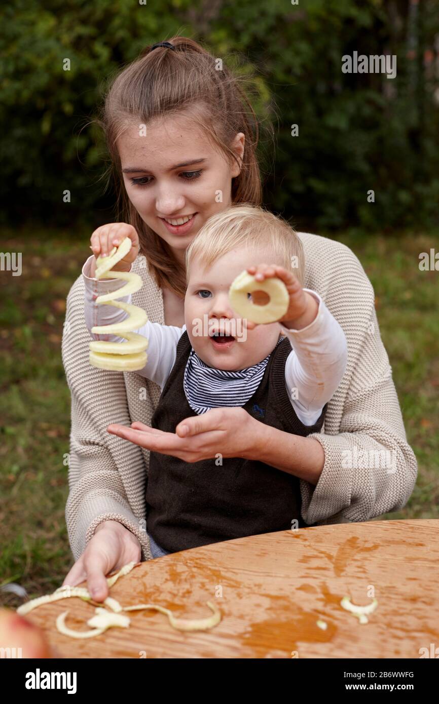 Children investigating food. Series: Apple Meadow Festival. A toddler admires apple rings. Learning according to the Reggio Pedagogy principle, playful understanding and discovery. Germany. Stock Photo