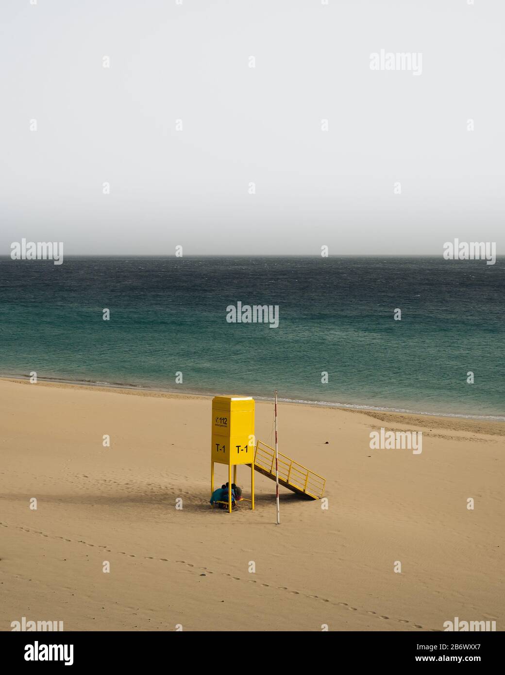 Very calm shot of beach with textured sand hills, blue water and yellow rescue post Stock Photo