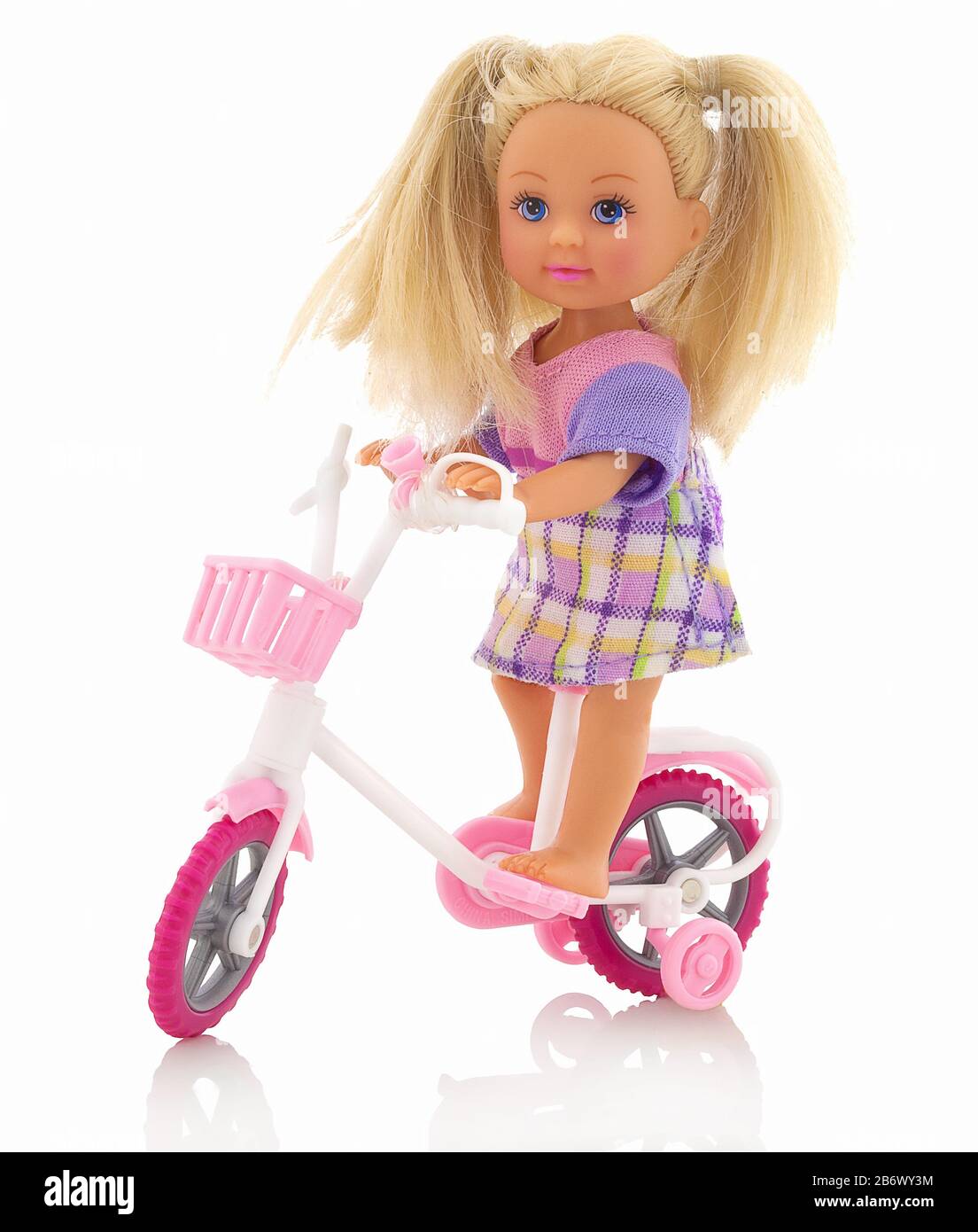 Small plastic baby girl toy on bicycle. Isolated on white background with shadow reflection. Girl toy on bike with auxiliary wheels and wire basket. C Stock Photo