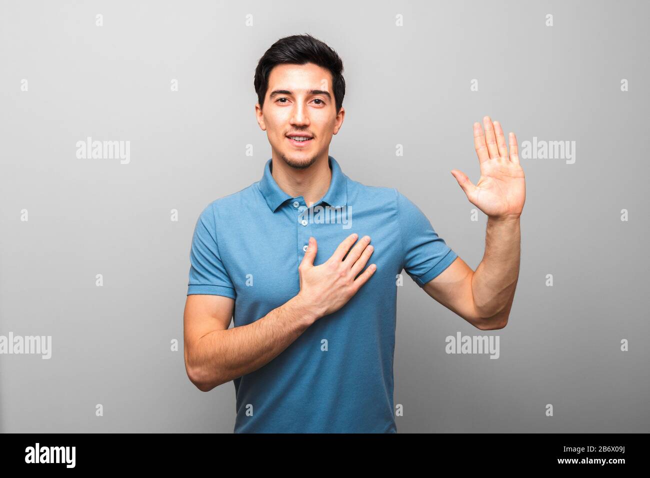 I swear. handsome young man in blue shirt with hand on chest giving oath against grey background. studio shoot Stock Photo