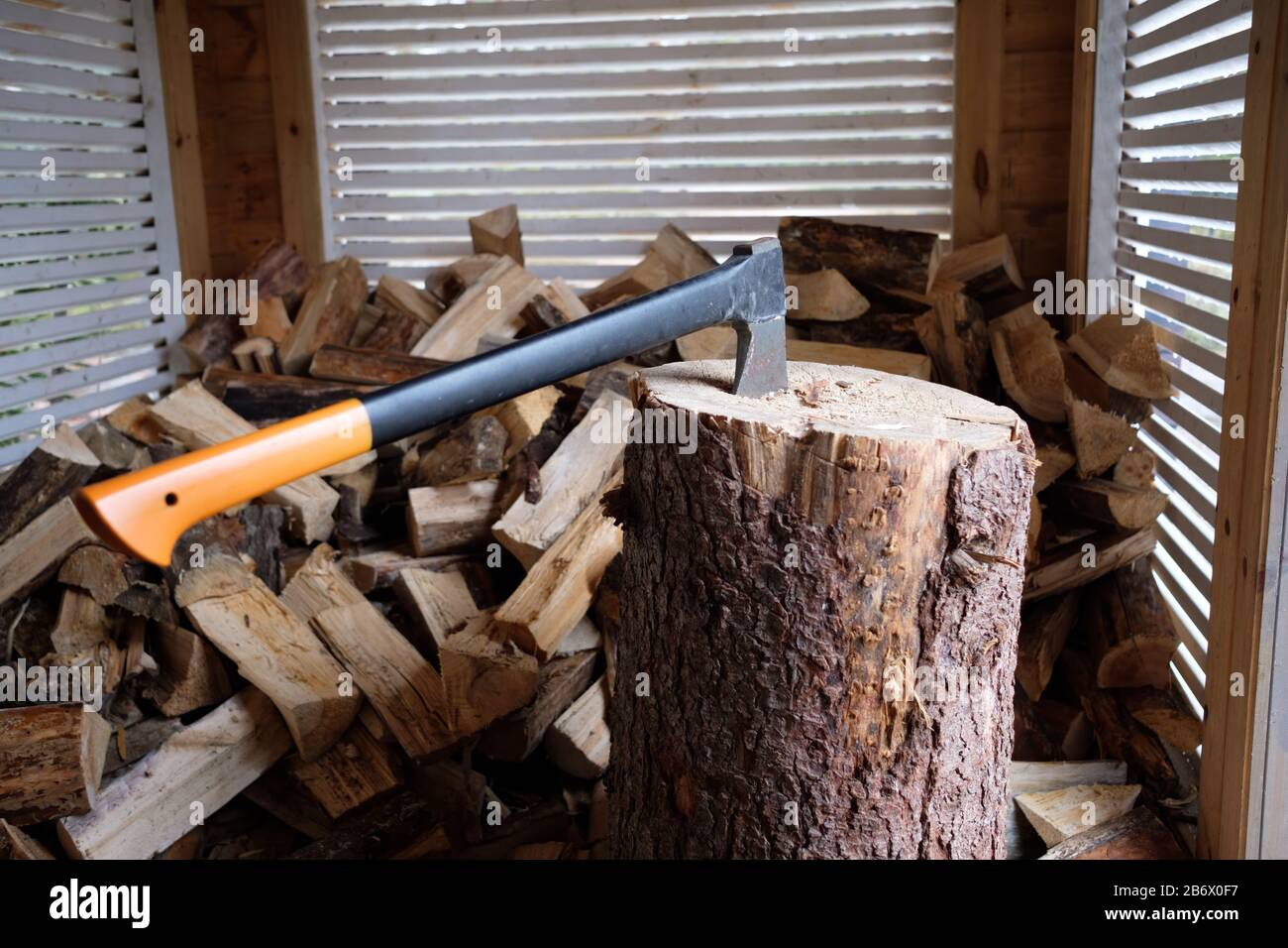 Close-up of axe ready for cutting logs. Cutting wood in the shed concept. Already chopped firewood laying in the background. Stock Photo
