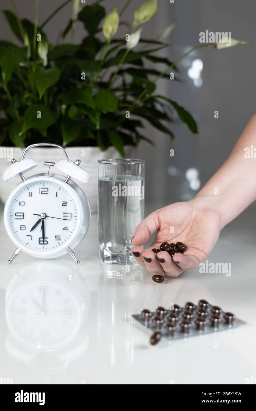 White alarm clock and medical pills with a glass of water on the table. Healthcare and medicine. Vitamins and mineral supplements in capsules. Stock Photo