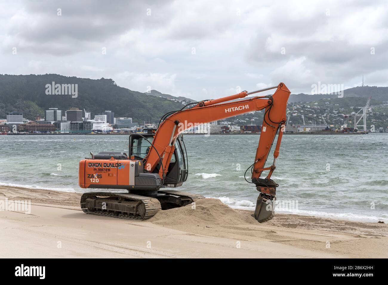 WELLINGTON, NEW ZEALAND - November 13 2019: cityscape with digger digging sand of bay shore beach at Oriental Parade neighborhood, shot in bright clou Stock Photo
