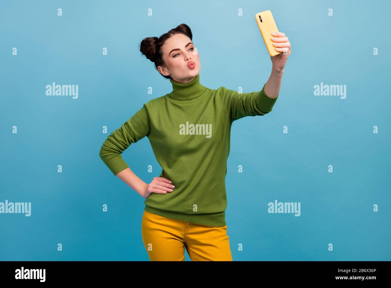 Photo of funny flirty lady hold telephone hand sending air kiss making selfies for boyfriend shooting for blog wear green turtleneck yellow pants Stock Photo