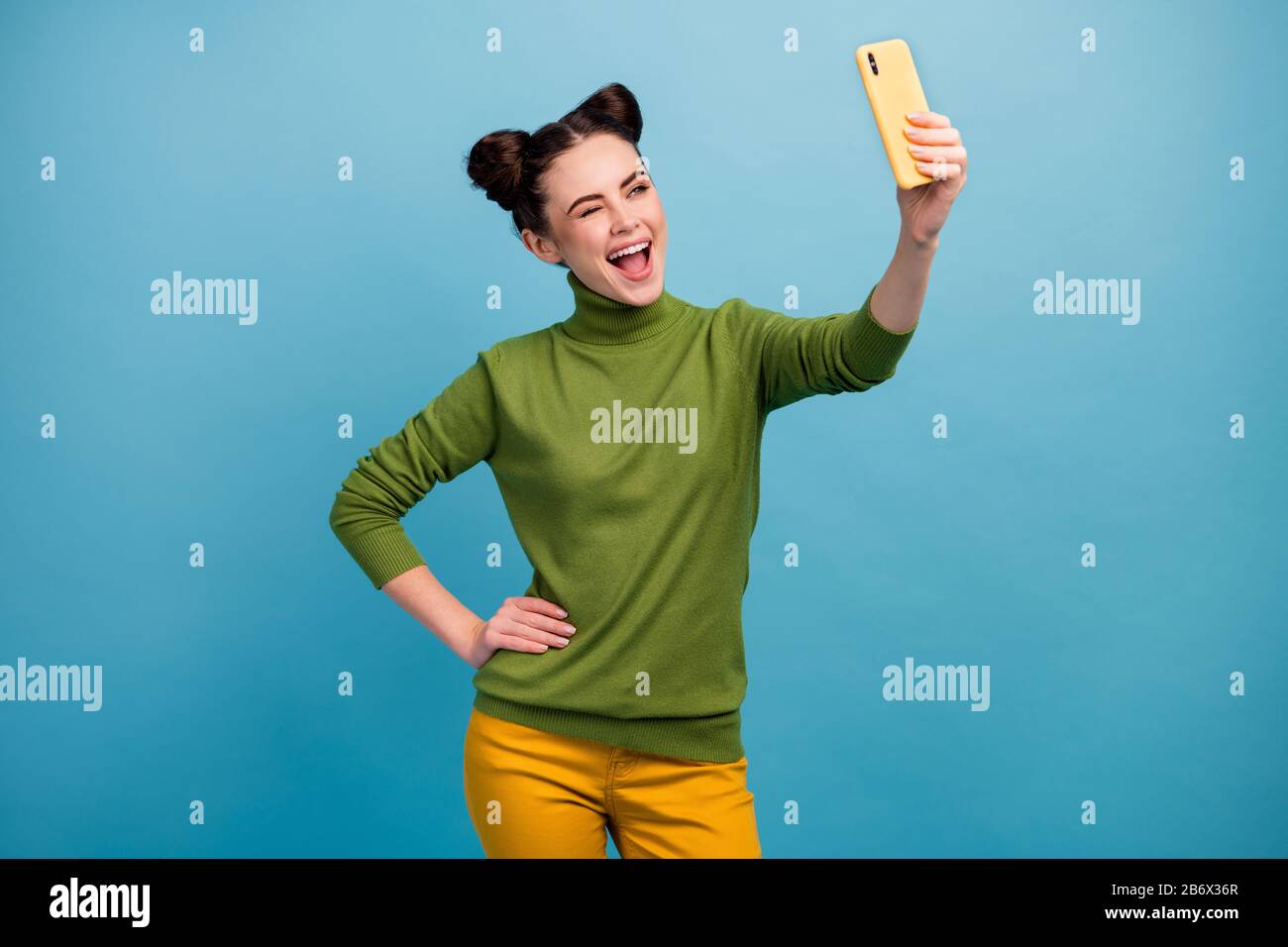 Photo of funny flirty lady hold telephone hand taking making selfies shooting for blog winking eye followers wear green turtleneck yellow pants Stock Photo
