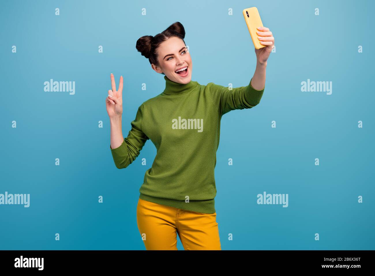 Photo of funny pretty lady hold telephone hand taking selfies shooting for blog showing v-sign symbol good mood wear green turtleneck yellow pants Stock Photo