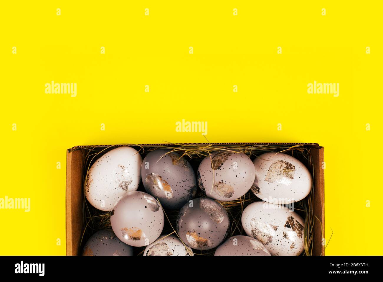 Silver painted decorative eggs in wooden box on bright yellow background. Easter concept. Place for text. Stock Photo
