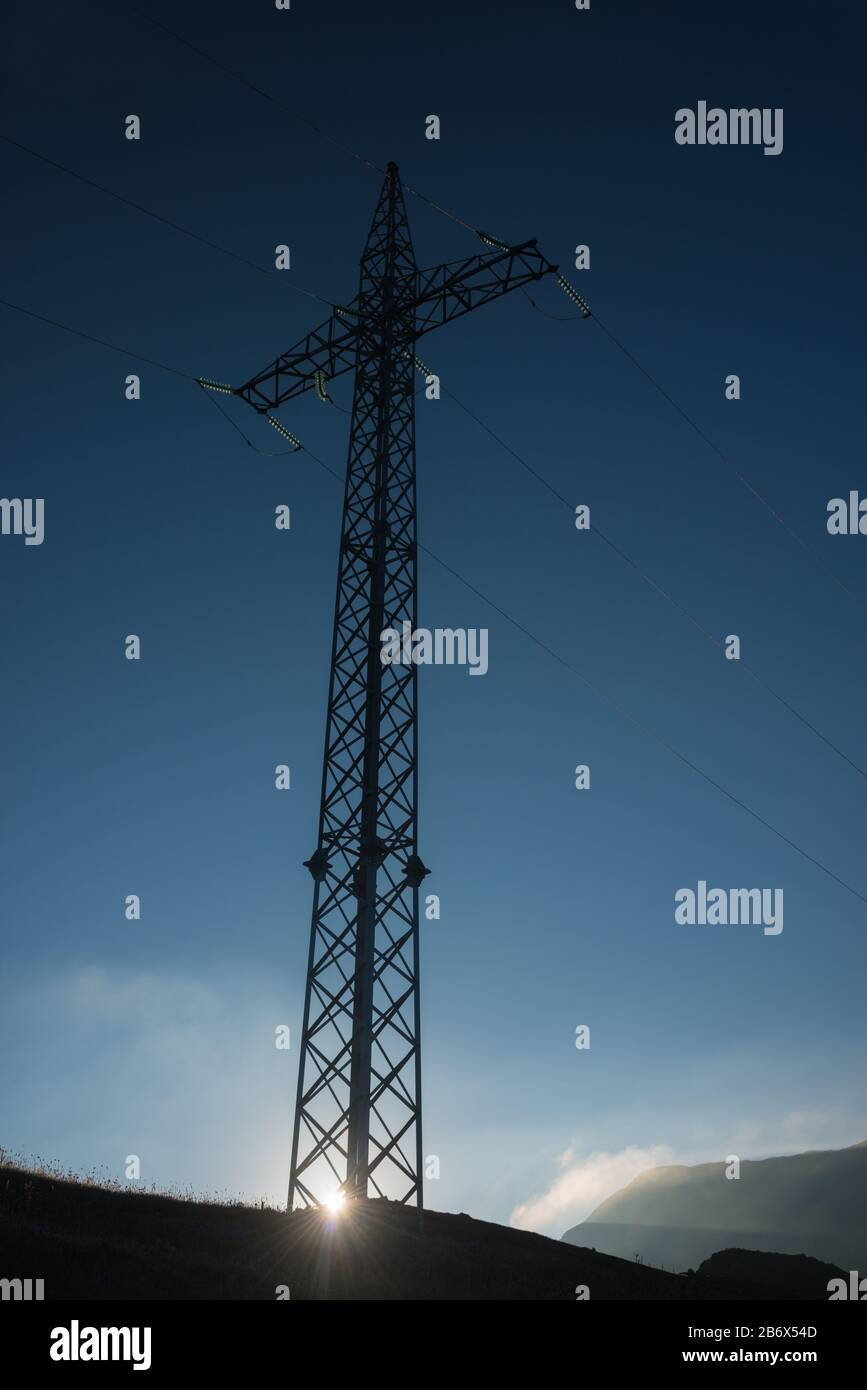 https://c8.alamy.com/comp/2B6X54D/high-voltage-power-line-pylon-against-blue-morning-sky-background-sunlight-penetrates-the-pylon-basement-object-is-situated-in-the-mountains-2B6X54D.jpg