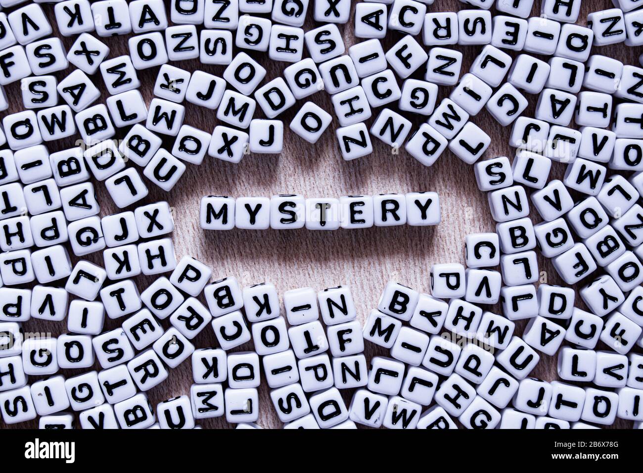 Word Mystery written in English with square and black letters mixed up with all the alphabet letters on a wooden board close-up. The other lette Stock Photo - Alamy