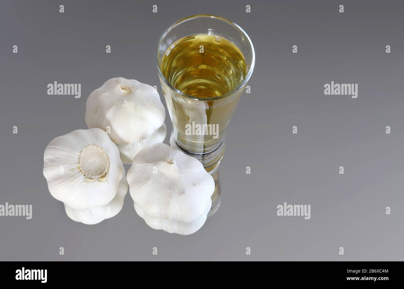 Garlic bulbs and garlic cloves on a mirror with a glass of alcohol