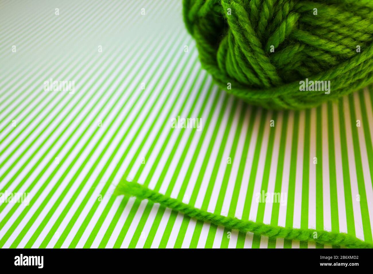 Green yarn ball on a green striped background. Stock Photo