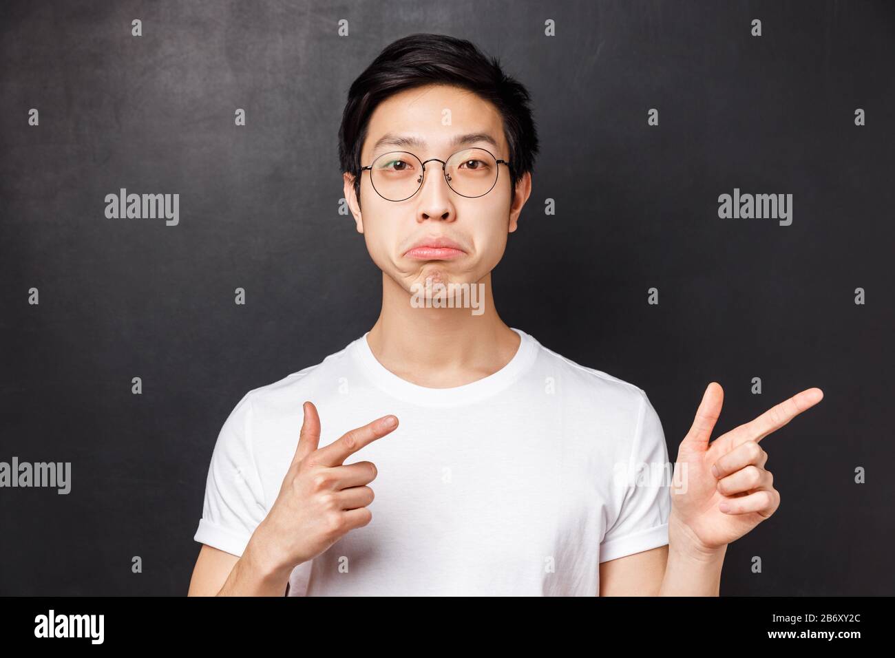 Close-up portrait of impressed asian man in glasses white t-shirt, pouting and looking camera with approval, pointing fingers right at really cool Stock Photo