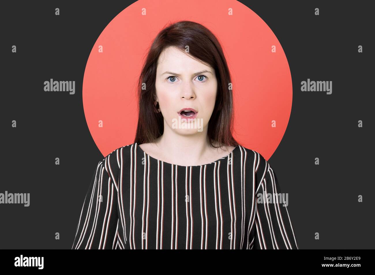 emotional astonished and shocked caucasian woman with open mouth and eyes wide open looking straight to the camera against a colored background Stock Photo