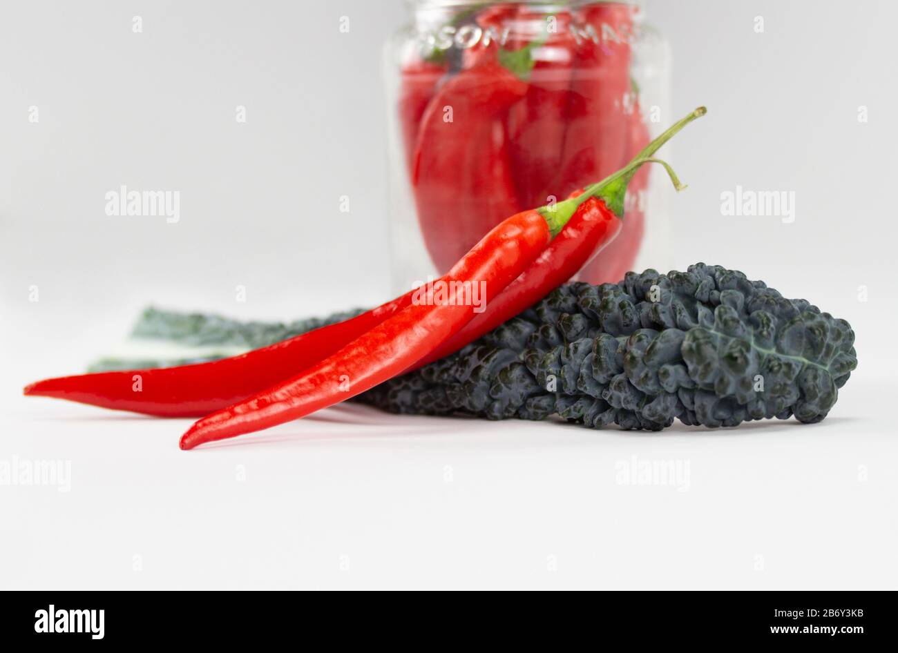 arrangement of red chili peppers and a lacinato kale leaf on white bakcground, also  called  dinosaur kale, flat kale, Tuscan kale or Italian kale Stock Photo